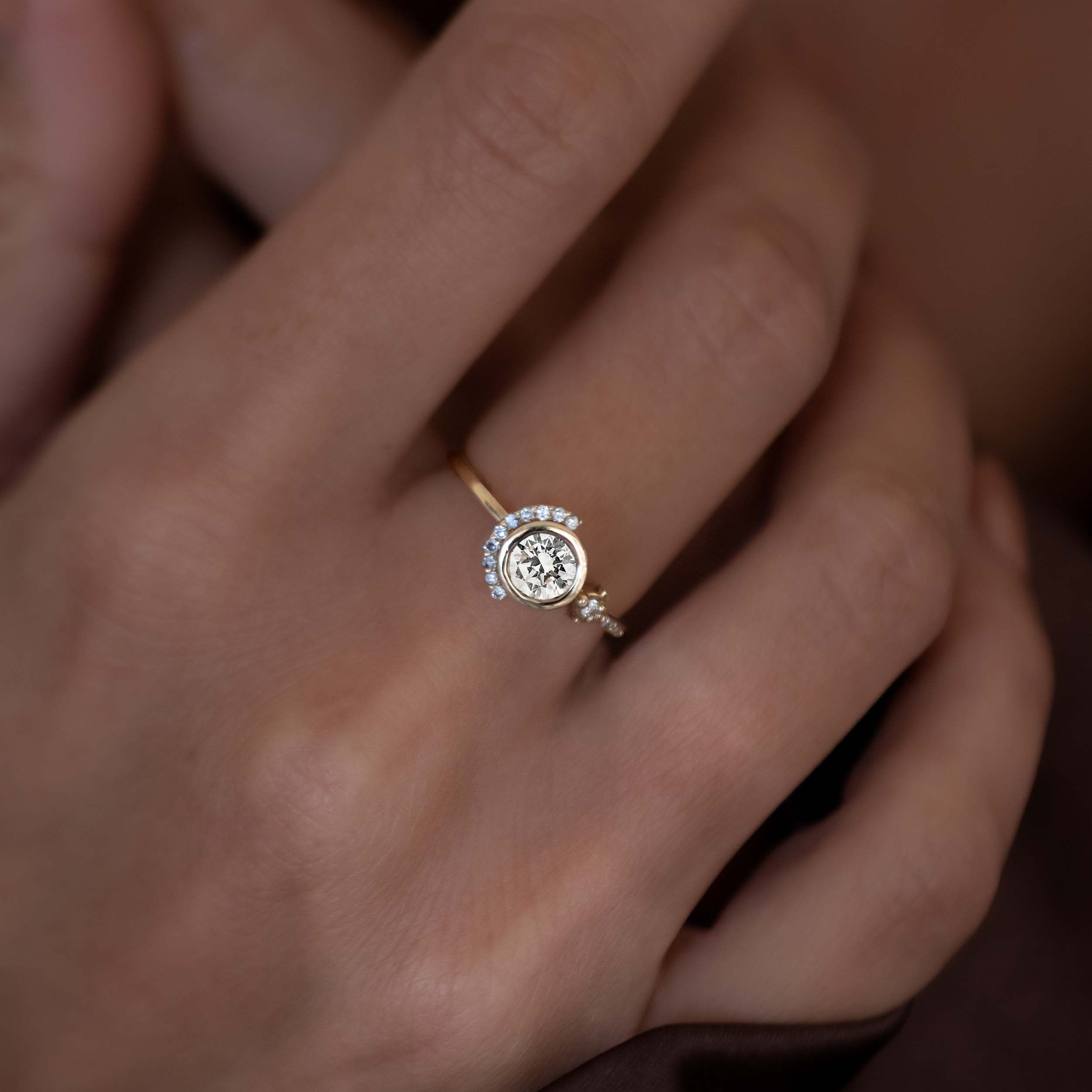 A diamond half moon engagement ring with a yellow gold band and bezel setting, featuring a central diamond surrounded by smaller side diamonds.